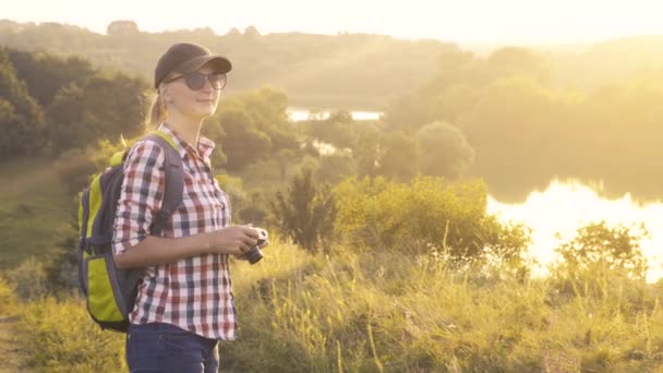 tourist girl with a backpack and a camera walks through a picturesque meadow and photographs the picturesque landscape. - Záběry, video