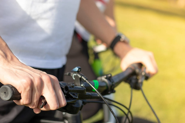 Close up of a mans hand holding onto the bicycle steering wheel, holding the brake pressed. Both hands seen, prepairing to start cycling outdoors - Photo, Image