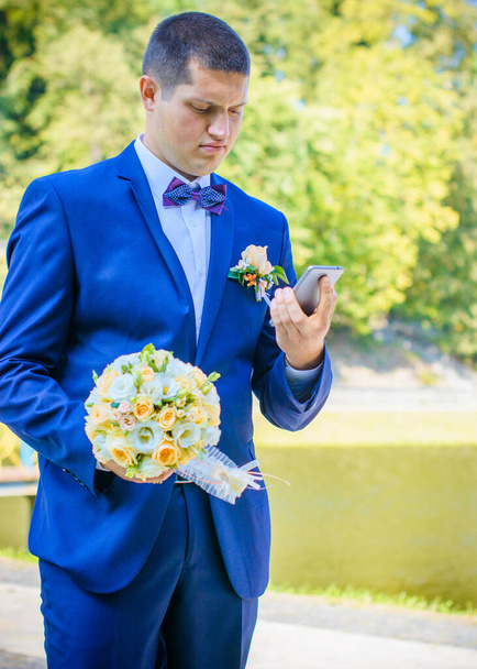 Ευτυχισμένος νεαρός γαμπρός στο πάρκο στο γάμο του - Φωτογραφία, εικόνα