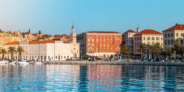 Όμορφη θέα του παραθαλάσσιου τμήματος, πεζόδρομος riviera του Σπλιτ της Κροατίας. Φωτεινή γαλάζια θάλασσα με φοίνικες και παλιά εκκλησιαστικά κτίρια κατά μήκος της περιοχής "Riva" - Φωτογραφία, εικόνα