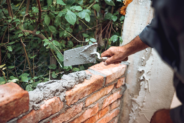 details of worker, bricklayer placing and adjusting bricks with mortar. Professional construction worker building exterior wall - Foto, Imagem