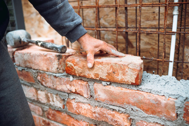 professional construction worker laying bricks and building walls on industrial construction site. Detail of hand adjusting brick - 写真・画像