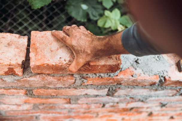 Close up of industrial worker, bricklayer installing bricks on construction site - 写真・画像