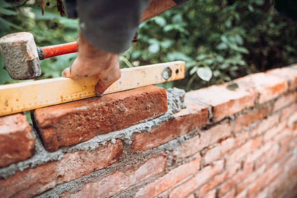 professional construction worker laying bricks and building walls in industrial site. Detail of hand adjusting brick - 写真・画像