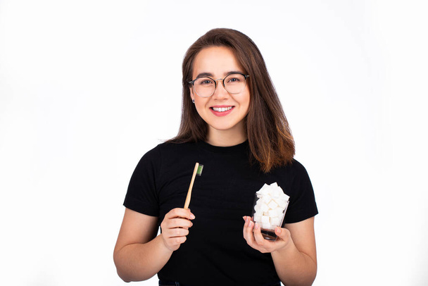 young beautiful woman holds a toothbrush and a glass with pieces of white sugar in her hands. oral care concept - Foto, afbeelding