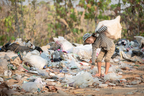 Egy szegény fiú szemetet gyűjt egy külvárosi hulladéklerakóból. Szegénység és gyermekmunka fogalma, emberkereskedelem.  - Fotó, kép