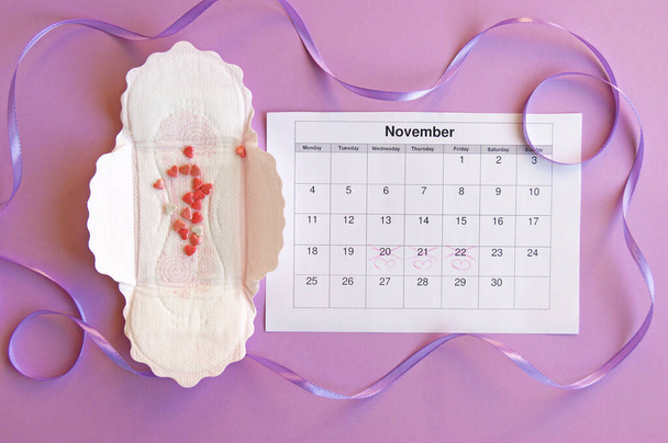 Menstruační polštářky a tampóny na menstruačním kalendáři na šeříkovém pozadí. - Fotografie, Obrázek