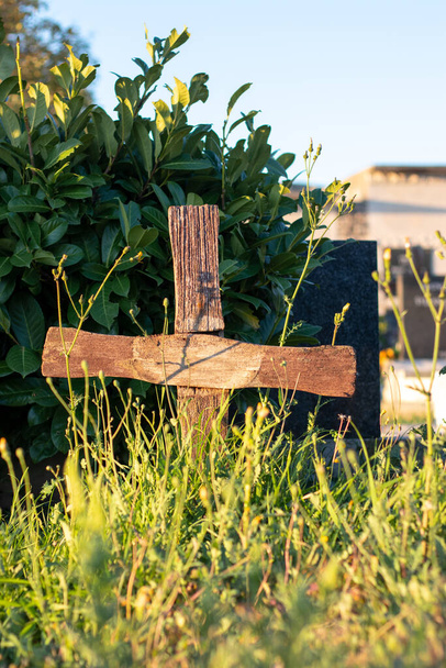 Старий коричневий хрест стоїть на невідомій могилі, переповненій травою і чагарниками. - Фото, зображення