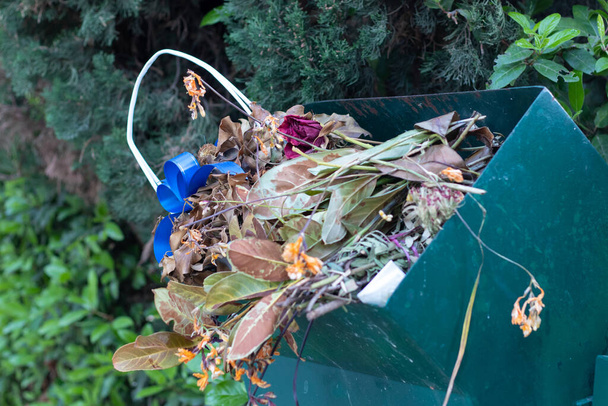 Groene vuilnisbak gevuld met gegooide bloemen en manden. Blijft over van het dagelijks onderhoud van het kerkhof. Vervanging van oude bloemen en besproeiing - Foto, afbeelding