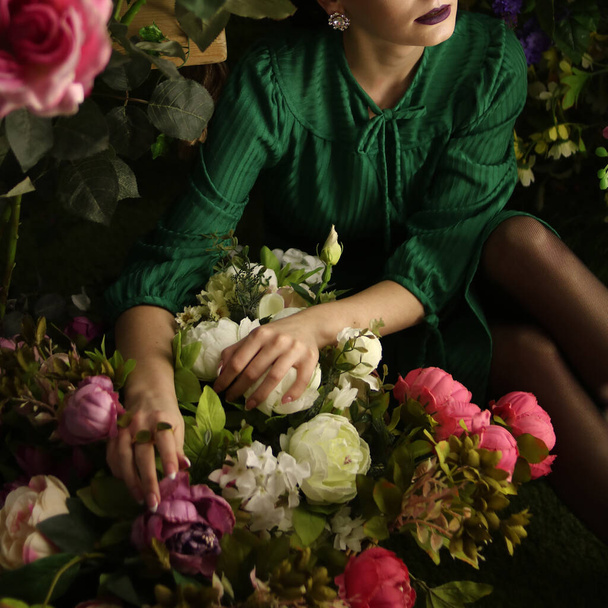 Girl in a green dress sits in a garden with flowers - Zdjęcie, obraz