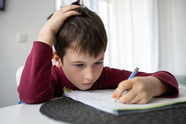 Portret młodego chłopca borykającego się z pracą domową. Koncepcja wychowania domowego dzieci. Kształcenie na odległość - Zdjęcie, obraz