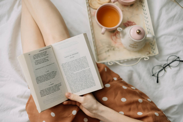 A woman reads a book at home in bed and drinks tea, home leisure in coziness and comfort. High quality photo - Valokuva, kuva