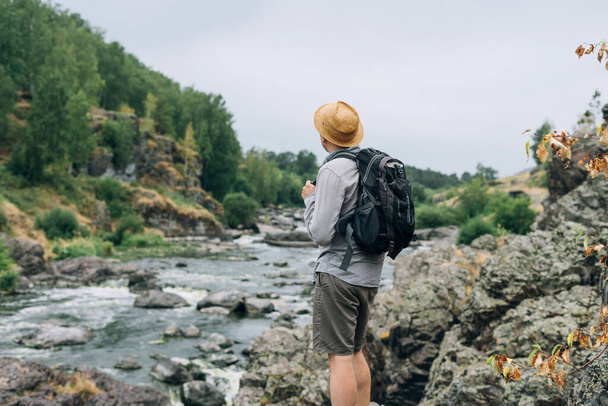 Молодий чоловік подорожує в солом'яному капелюсі з рюкзаком на гірській річці, місцеві подорожі та концепція подорожі на вихідні
 - Фото, зображення