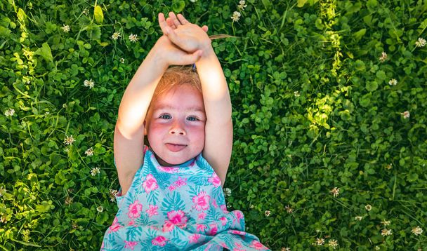 Bella bambina sdraiata sull'erba ridendo e guardando in alto. 2-3 anni bambino in natura nella soleggiata giornata estiva - Foto, immagini