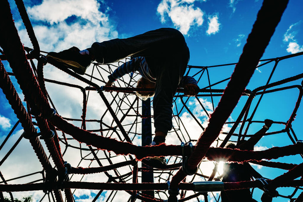 Silueta de niños jugando en un parque, trepando sobre unas cuerdas viviendo aventuras
. - Foto, imagen