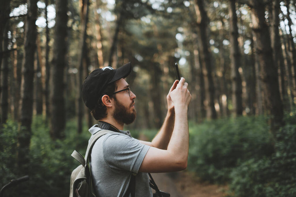 Een jonge mannelijke toerist maakt foto 's op een smartphone camera in een bos. Toerisme, actieve levensstijl. Hoge kwaliteit foto - Foto, afbeelding