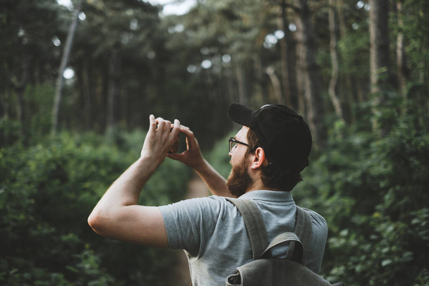 Genç bir erkek turist ormandaki akıllı telefon kamerasıyla fotoğraf çekiyor. Turizm, aktif yaşam tarzı. Yüksek kalite fotoğraf - Fotoğraf, Görsel