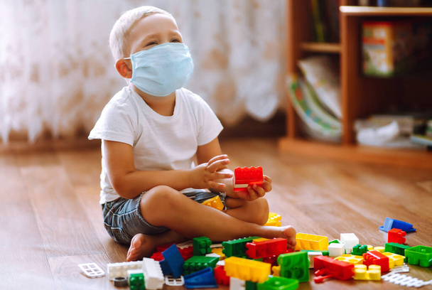 Little boy in sterile medical mask  playing constructor at home. The concept of preventing the spread of the epidemic. - Fotoğraf, Görsel