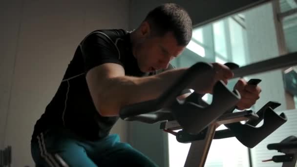 Blanc sportif tourbillonnant pédales sur un vélo stationnaire dans une salle de gym - Séquence, vidéo