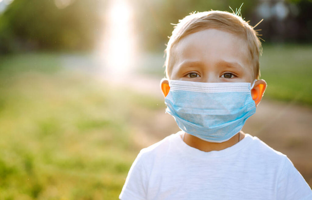 Portrait of little boy with medical face mask in the park during pandemic. Concept of health and safety life from coronavirus. Covid-2019. Kids safety. - Foto, afbeelding