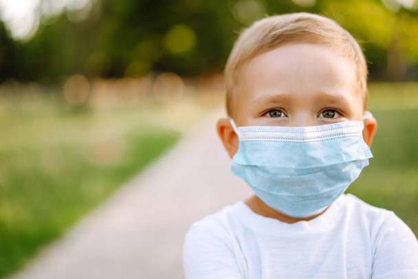 Portrait of little boy with medical face mask in the park during pandemic. Concept of health and safety life from coronavirus. Covid-2019. Kids safety. - Fotoğraf, Görsel