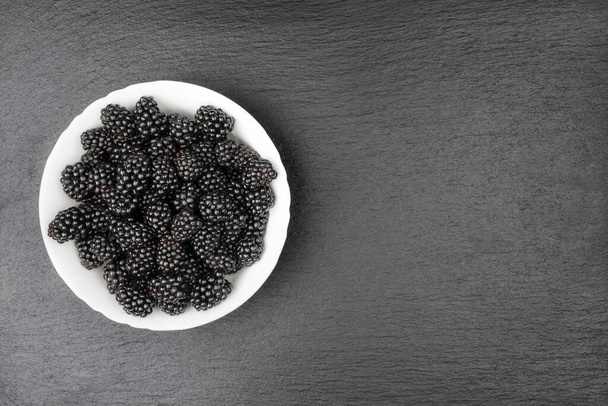 Blackberries in a white bowl on a slate slab - Φωτογραφία, εικόνα