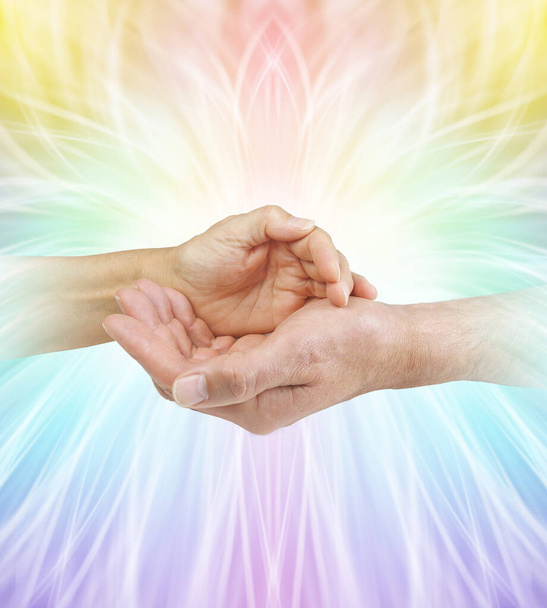 Our energies together are a formidable force - female hand cupped over a male cupped hand against a rainbow coloured symmetrical outwardly flowing energy formation background with copy space                              - Foto, Imagem