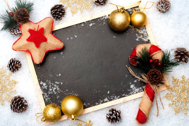 雪の白い背景に枝、素朴な星と繊維のキャンディーの杖とヴィンテージブラックボードのトップビュー。コピースペースと散在の雪に覆われたクリスマスの装飾とレトロなスレートの黒板 - 写真・画像