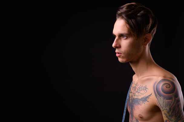 Studio shot of young handsome rebellious man shirtless against black background - Фото, изображение