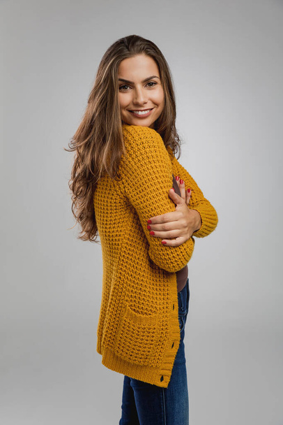 Beautiful and confident young woman against gray background in studio weaning yellow cardigan sweater  - Foto, Bild