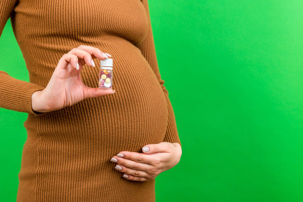 Großaufnahme einer Flasche Vitamintabletten in der Hand einer schwangeren Frau vor buntem Hintergrund mit Kopierraum. Gesundheitskonzept. - Foto, Bild