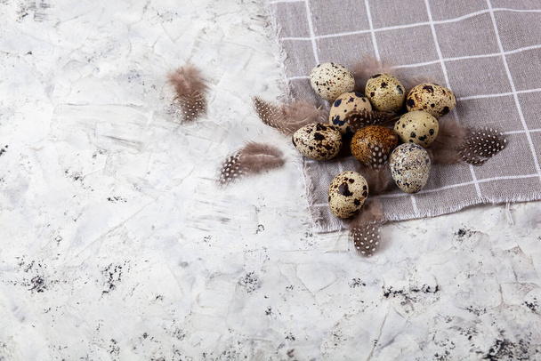 pile of Easter quail eggs on gray fabric rag on white concrete background. space for text - Photo, Image