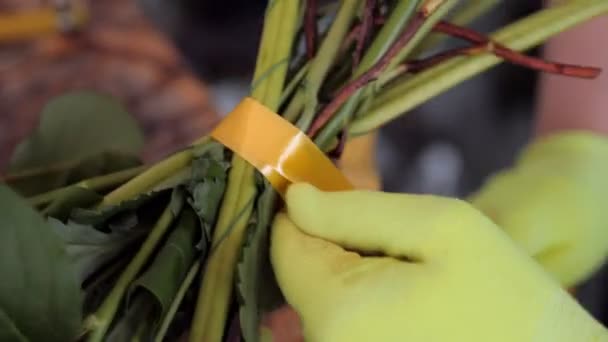 florist ties flower bouquet with golden ribbon in shop - Materiał filmowy, wideo