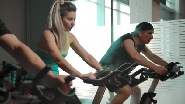 Sportowe osoby rasy kaukaskiej, dwóch mężczyzn i jedna kobieta na rowerze symulator - Materiał filmowy, wideo
