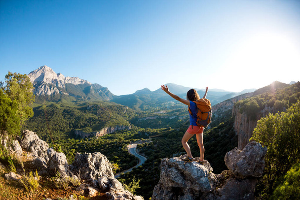Uma mulher com uma mochila fica no topo de uma montanha com as mãos para cima e admira a beleza de um vale, A menina viaja para lugares bonitos, Alcançando o objetivo, Bela paisagem da Turquia. - Foto, Imagem