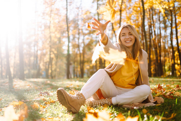 Очаровательная молодая женщина веселится с листьями в осеннем парке. Красивая девушка бросает жёлтые листья. Отдых, отдых, концепция образа жизни. - Фото, изображение