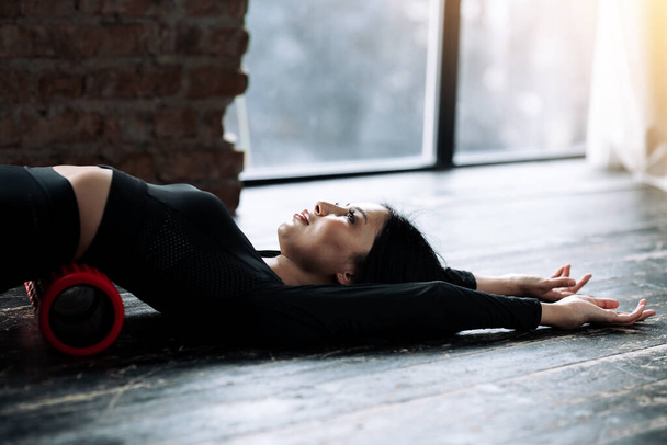 The upper part of the body of a girl massaging the fascia of the lumbar muscles stretching her arms along the wooden floor in the gym - Foto, Bild