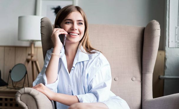 Young cheerful woman talking on mobile phone at home. - Foto, Imagen