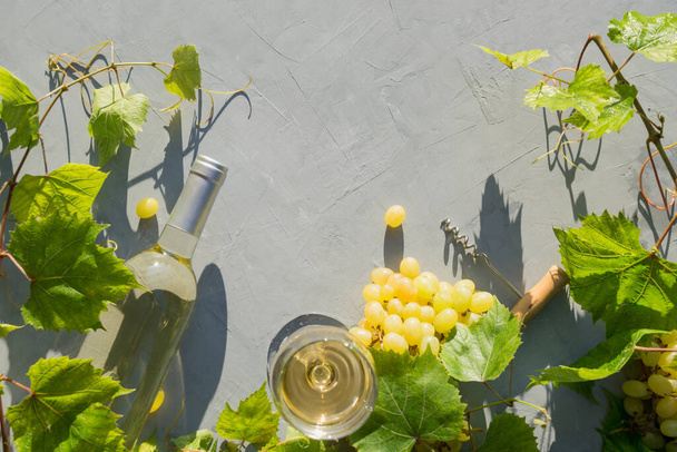 White wine with bottle and wineglass, ripe grape on grey table. View from above. Outdoors. Space for text. - Foto, imagen
