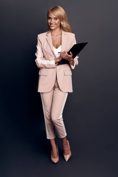 Selbstbewusste junge Frau in schicker Freizeitkleidung mit Tablet vor grauem Hintergrund. - Foto, Bild