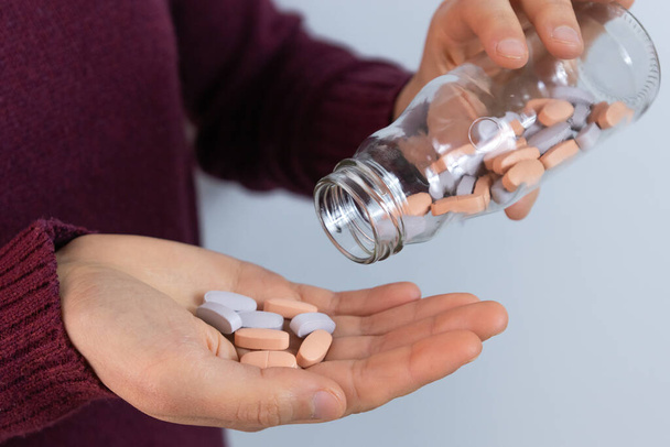 Крупним планом жіночі руки з пляшкою таблеток і деякими таблетками в руці. Горизонтальне зображення з білим тлом
. - Фото, зображення