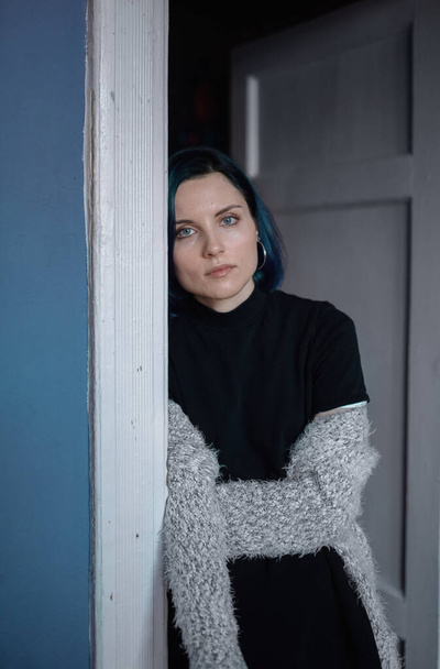 Egy fekete ruhás fiatal lány áll egy kék falú nappali ajtajában. - Fotó, kép