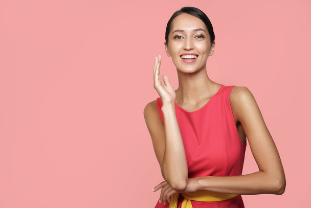 Onnellinen nainen vaaleanpunaisessa mekossa vaaleanpunaisella taustalla. Valoisa studio valokuva - Valokuva, kuva