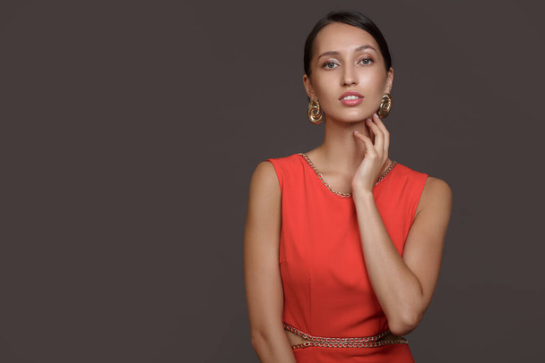 Fashion brunette woman in red dress and gold earrings. Touching your hand to your face. Copycpase - Photo, Image
