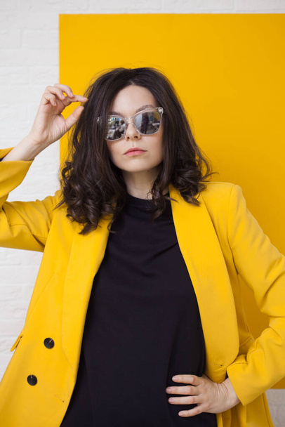 stylish and daring young brunette in a bright yellow jacket and mirrored sunglasses. - Foto, Bild