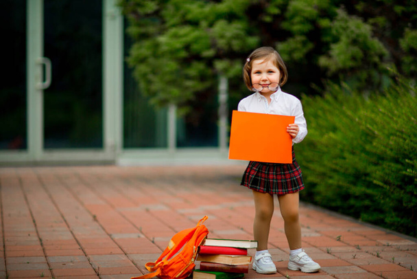 a girl in a school uniform stands near the school, with a piece of paper, a layout with space for text and copying - 写真・画像