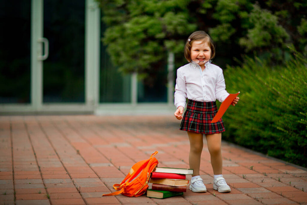 a girl in a school uniform stands near the school, with a piece of paper, a layout with space for text and copying - Foto, Imagem