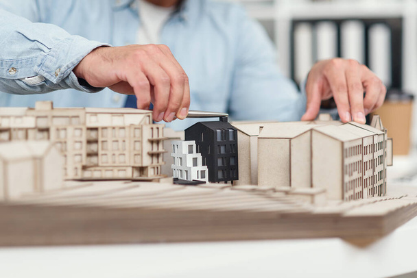 Close up architects hands constructing model of buildings and examines his work. Urban architecture and design concept. - Fotografie, Obrázek