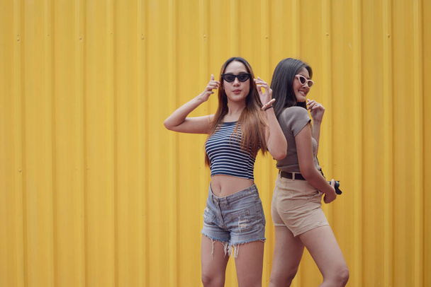 Fiatal ázsiai örömteli pár nők nyári divat lakosztály áll sárga acél lemez háttér. Fogalom boldog és szép élet tinédzser. - Fotó, kép
