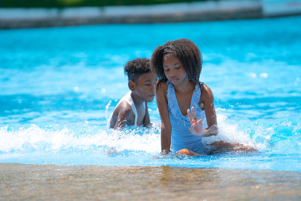 African girl and boy sitting and playing water in swimming pool at amusement park.  Concept kid are expressing pure joy and excitement - Photo, Image